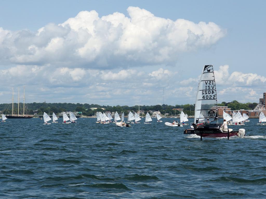 a fleet of kids in sailing prams (accompanied by instructors in motorboats) trains at Newport Harbor